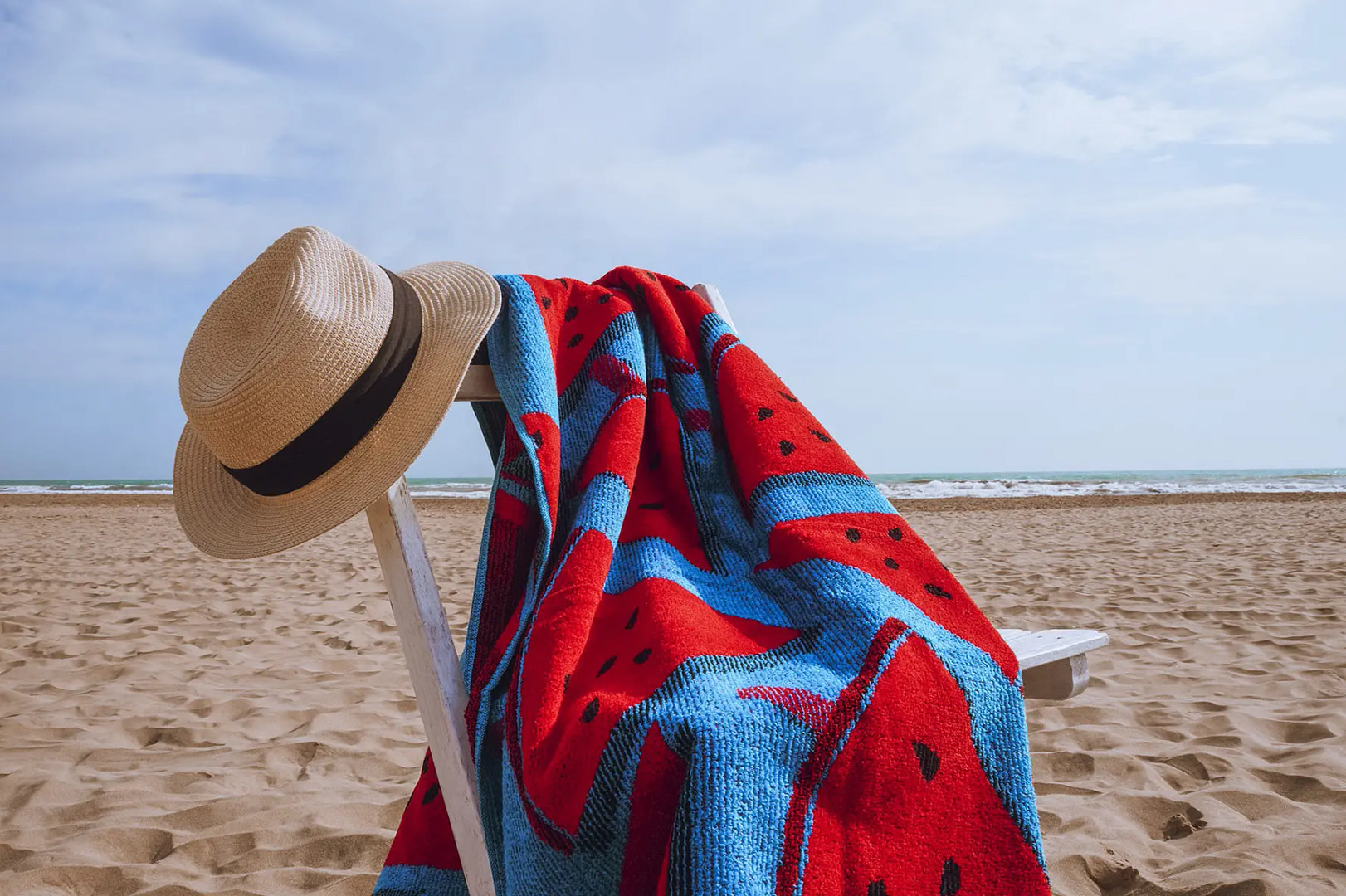 toalla con estampado de sandias encima de una silla rustica en la playa